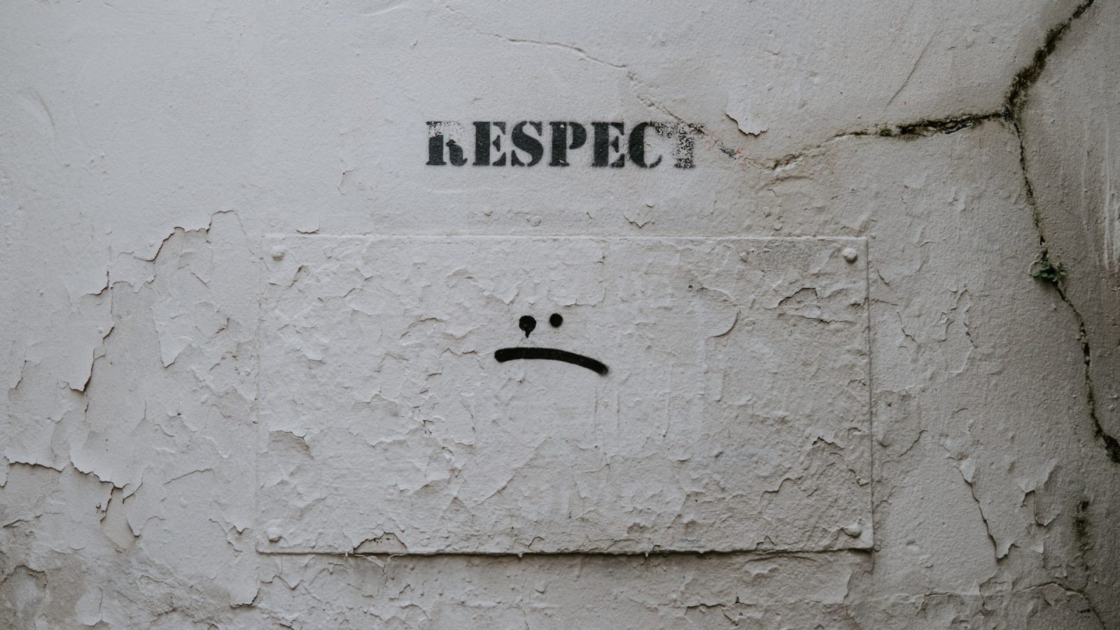 Wall showing graffiti that reads "respect" with a sad face below it